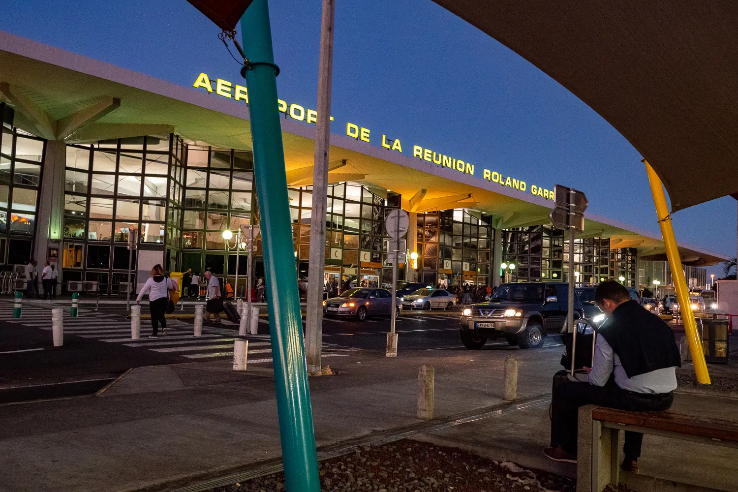 Abflugterminal bei Dämmerung mit beleuchtetem Schild und wartenden Fahrzeugen