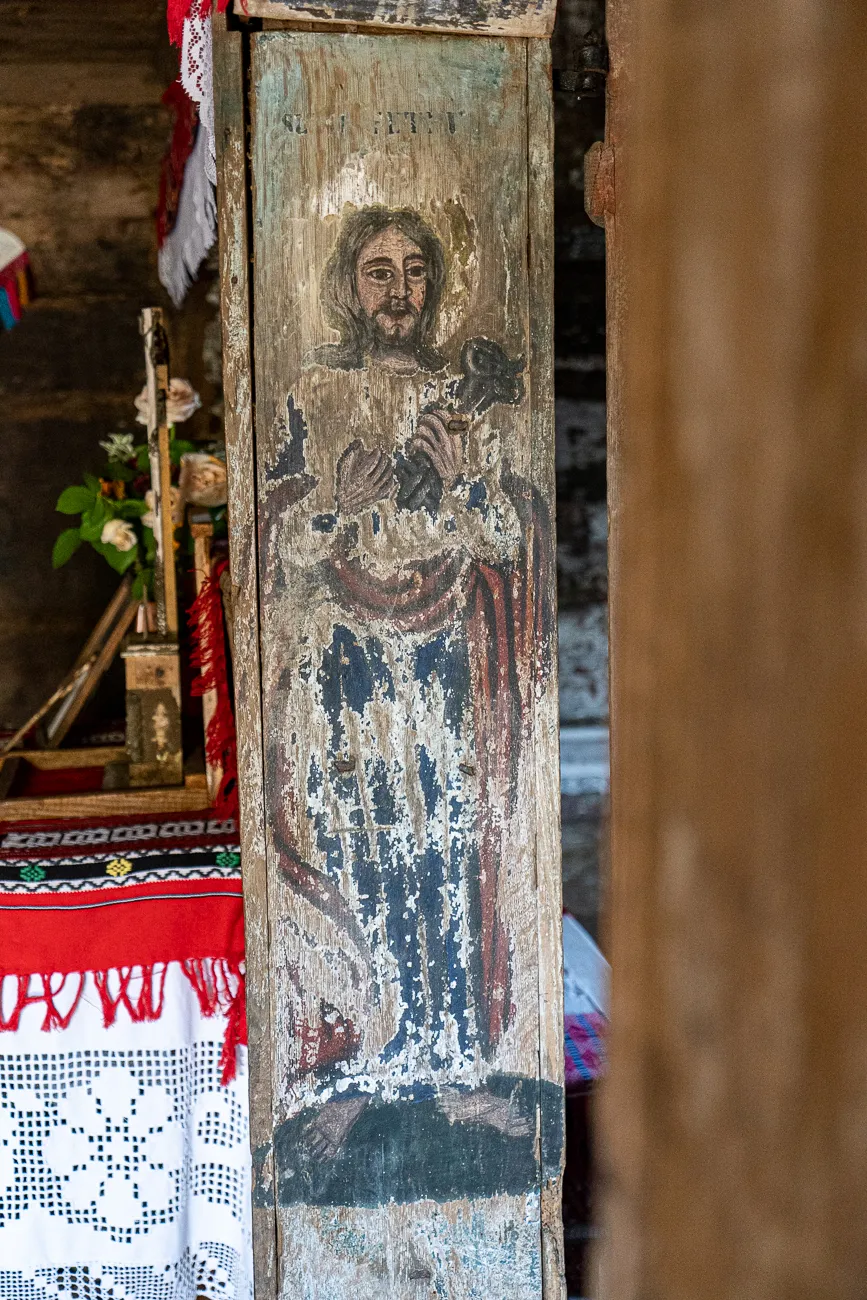 Alter Holzbild mit Jesusfigur in Kirche, umgeben von Stickerei und Blumen.