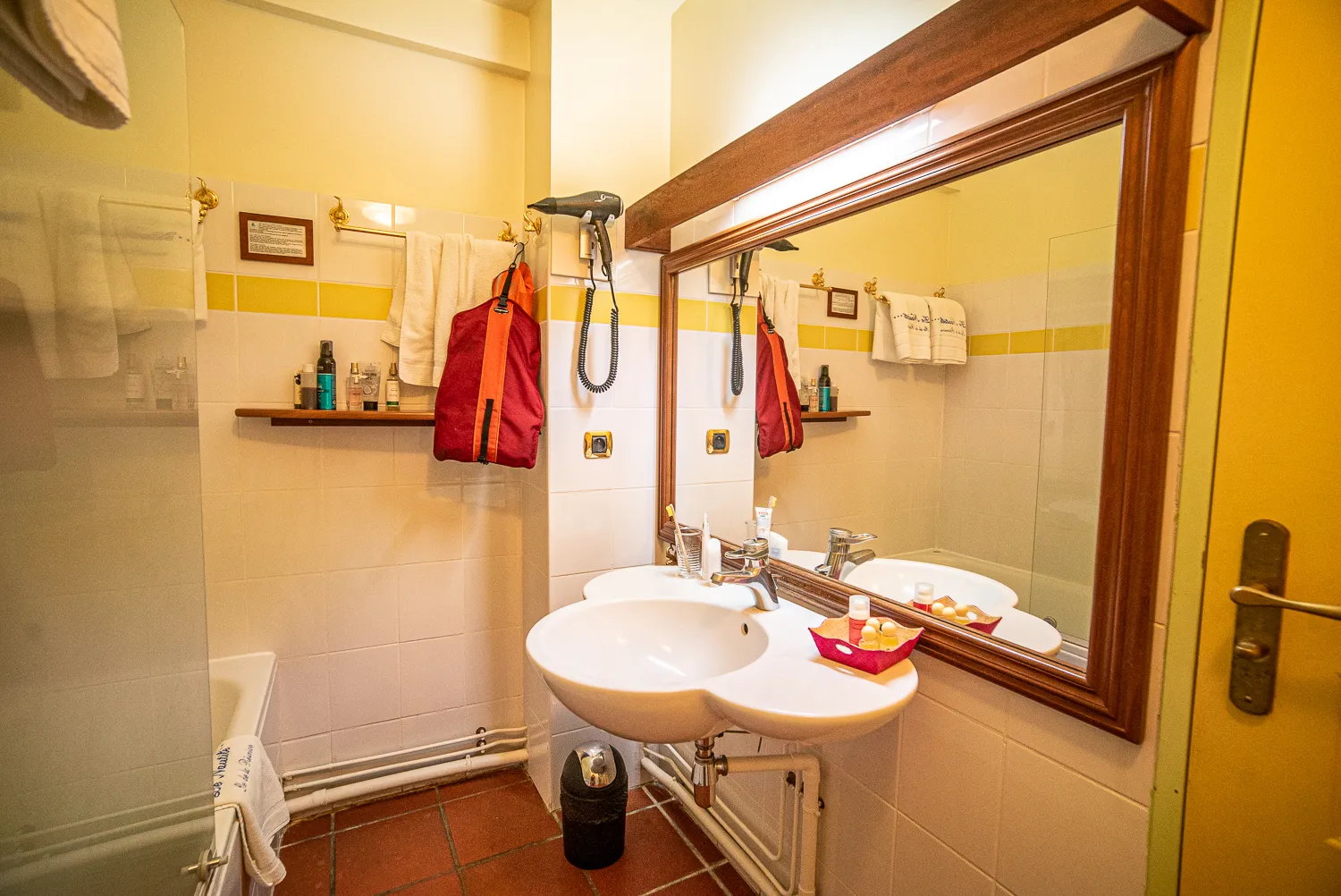 Badezimmer mit Spiegel, Waschbecken und rotem Rucksack an der Wand.