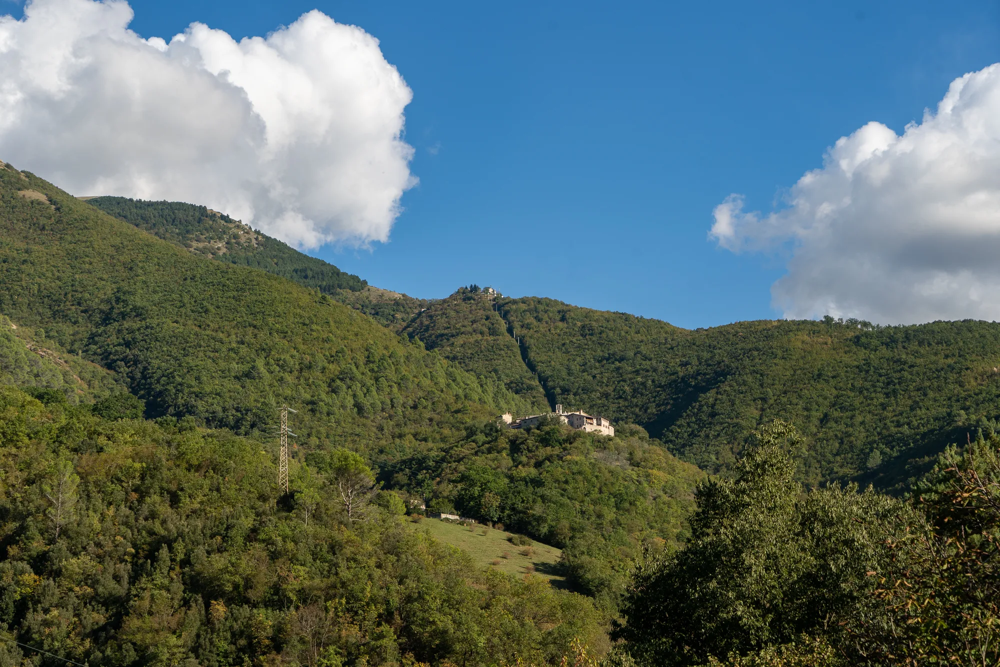 Berg mit bewaldeten Hängen und historischem Gebäude unter blauem Himmel