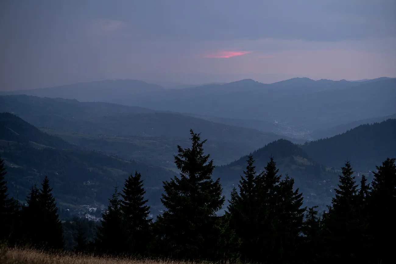 Dämmerung über bewaldeten Bergen mit rosa Farbton am Horizont