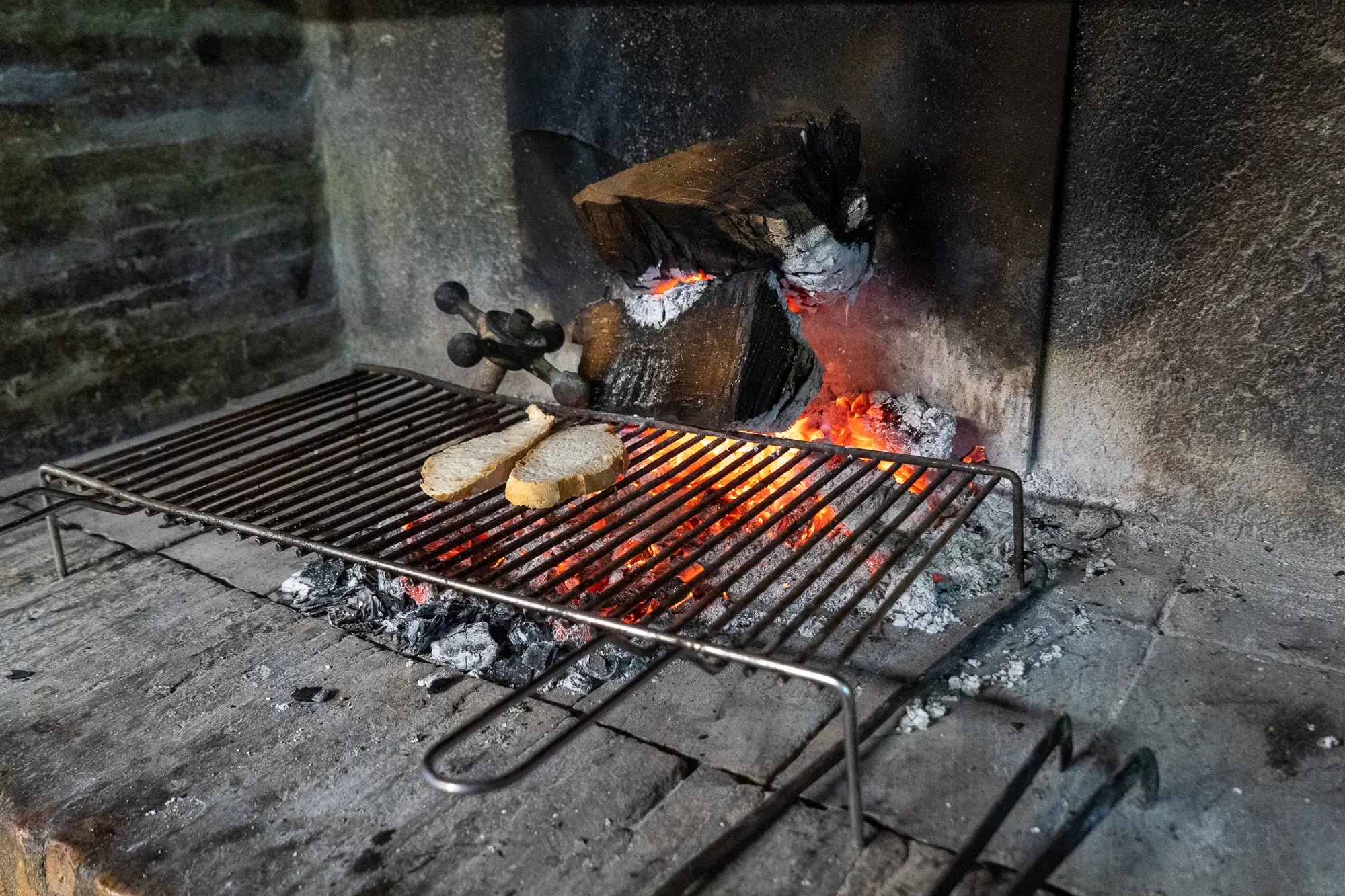 Zwei Scheiben Brot auf einem Grillrost über glühenden Kohlen in einem Ofen.
