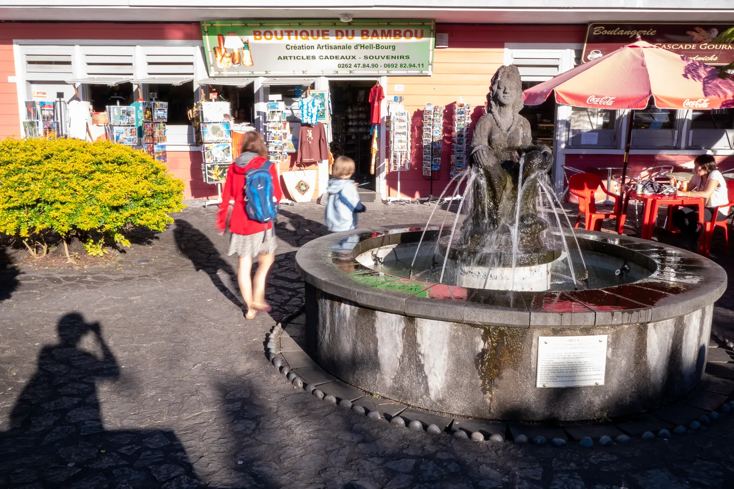 Brunnen mit Statue, Geschäfte und Passanten im Hintergrund