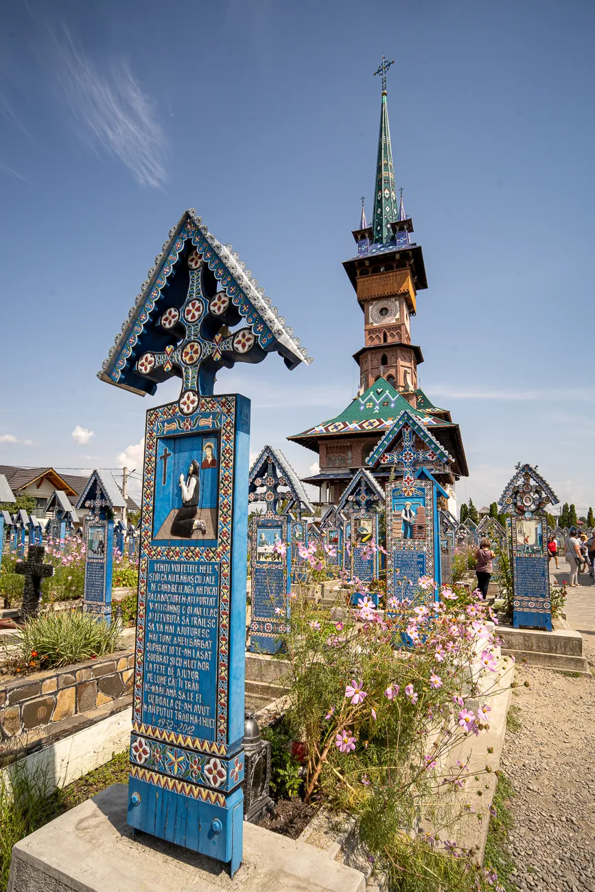 Bunt bemalter Holzkreuz und Kirche im Friedhof unter blauem Himmel