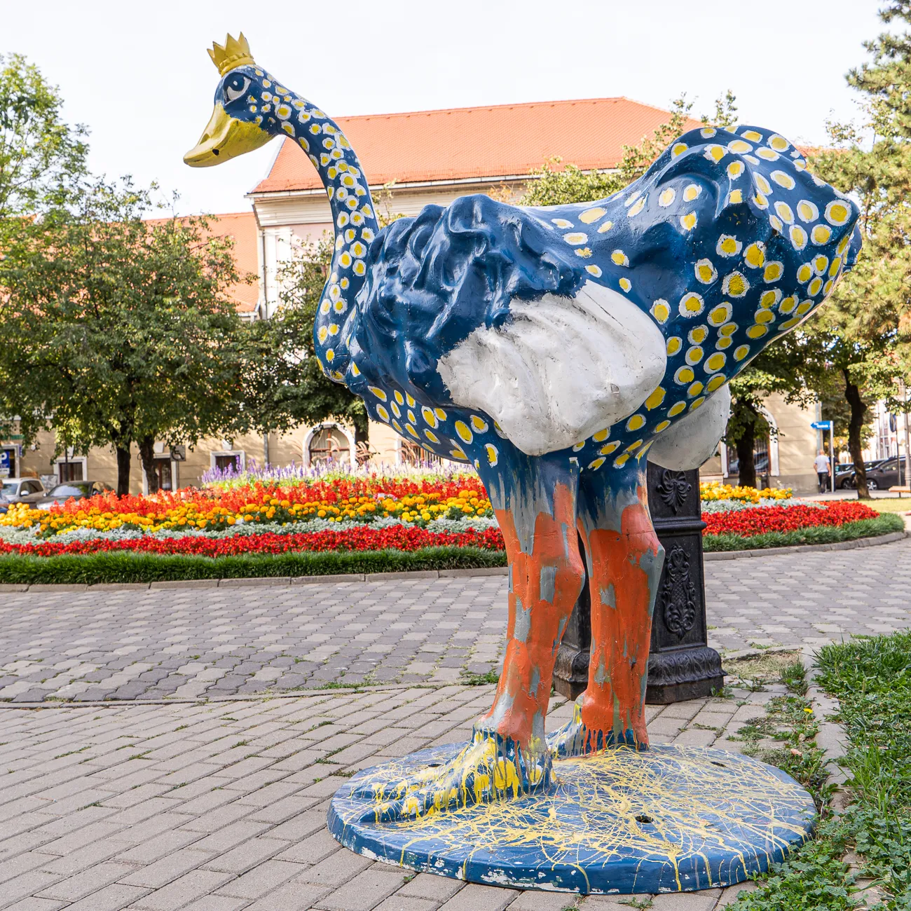 Farbige Entenskulptur mit Krone vor Blumenbeete und Gebäude