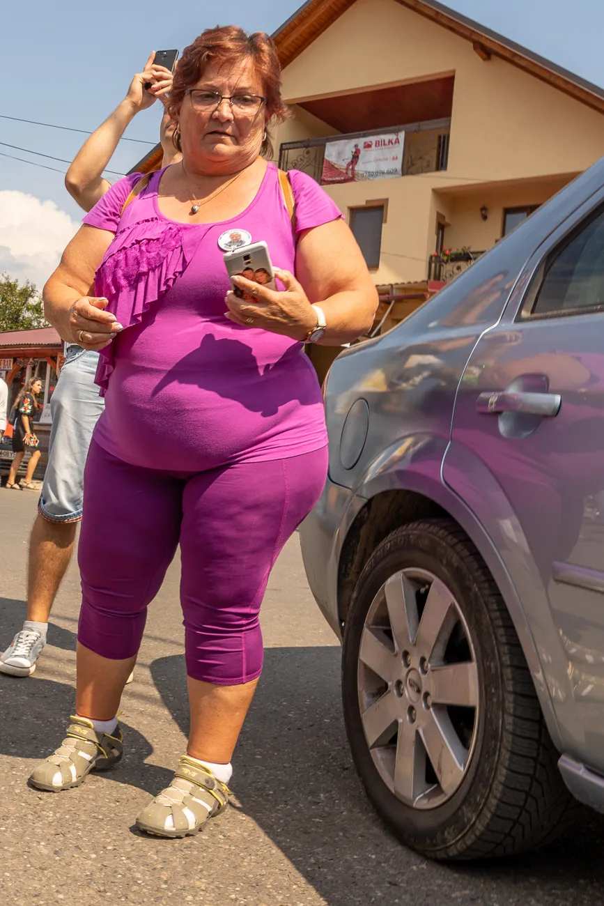 Frau in lila Kleidung hält Smartphone, steht neben silbernen Auto