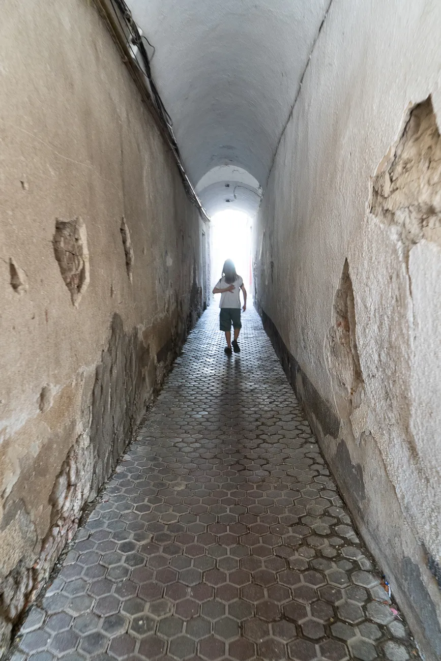 Mensch geht durch enge, gewölbte Gasse mit hexagonalem Bodenbelag