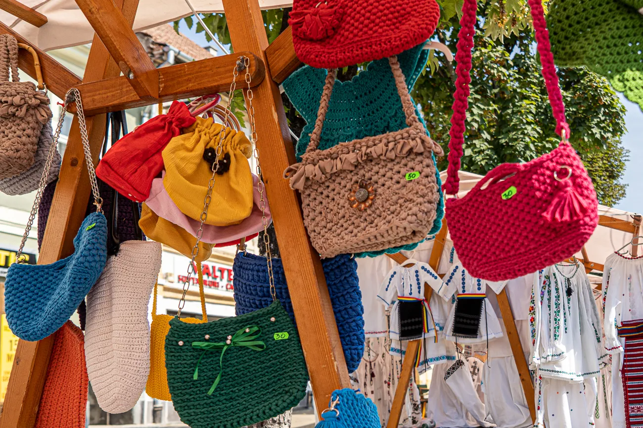 Farbige gehäkelte Taschen und Kleidung an einem Marktstand