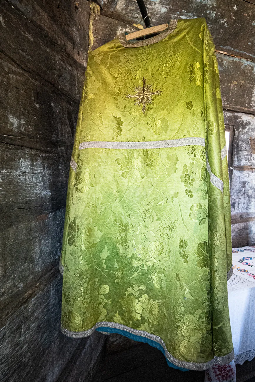 grün-goldener liturgischer Gewand mit Kreuz und Blumenmuster an Holzwand