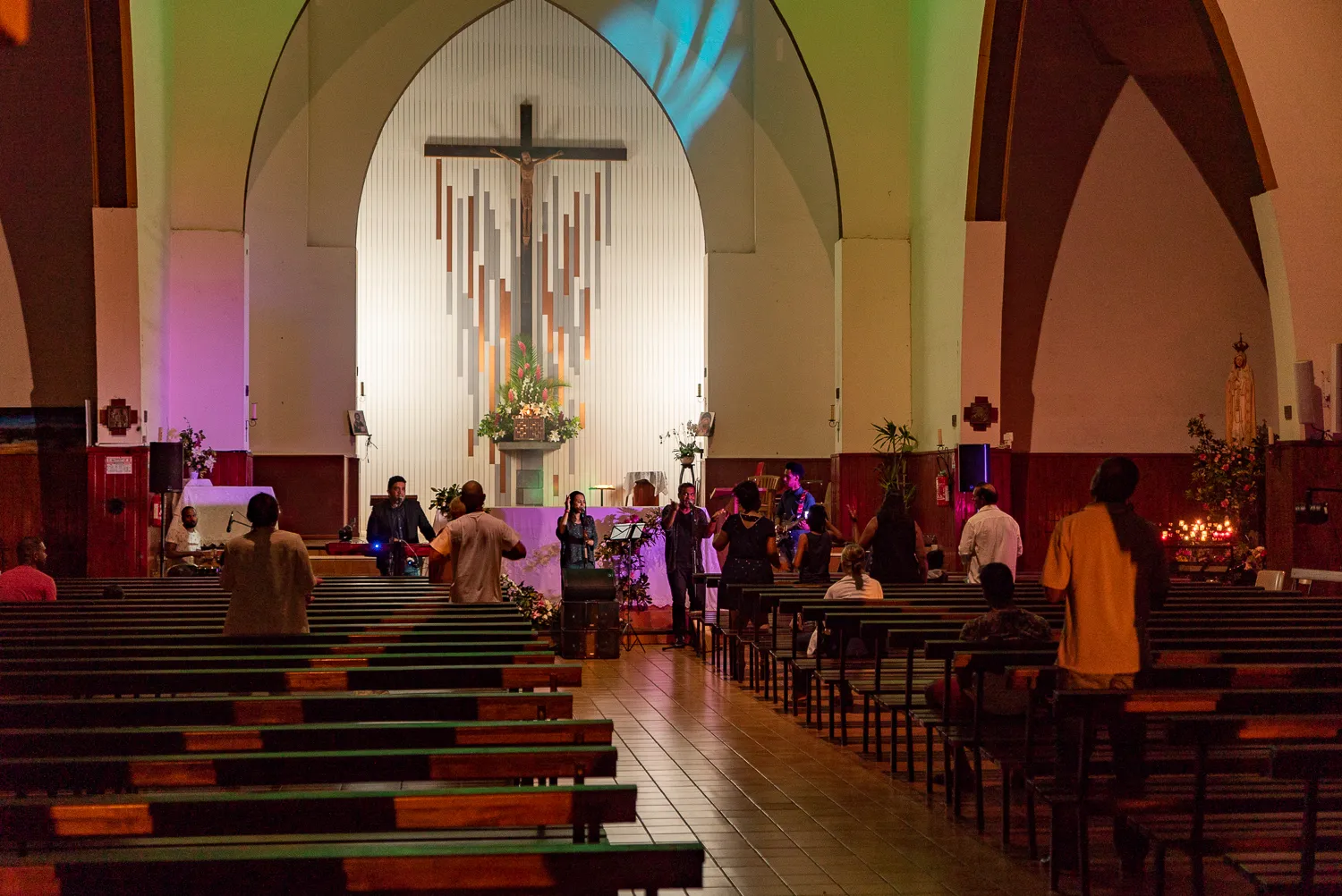Innenansicht einer Kirche mit Kreuz, Bänken und Menschen bei einem Gottesdienst