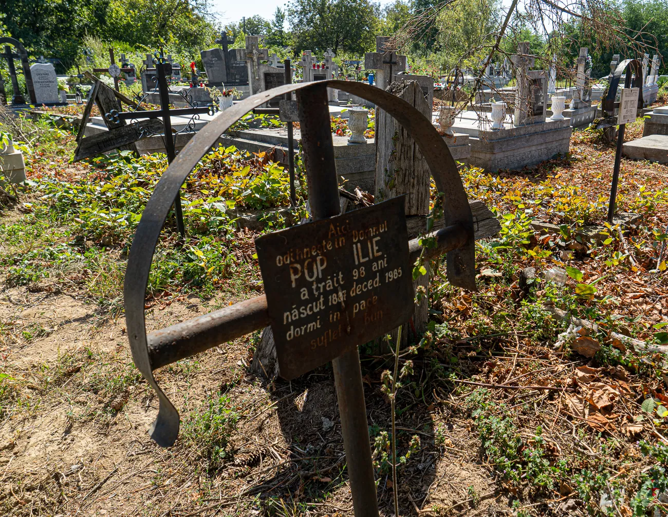 Rostige Metallkreuz mit Grabstein im Friedhof unter Bäumen