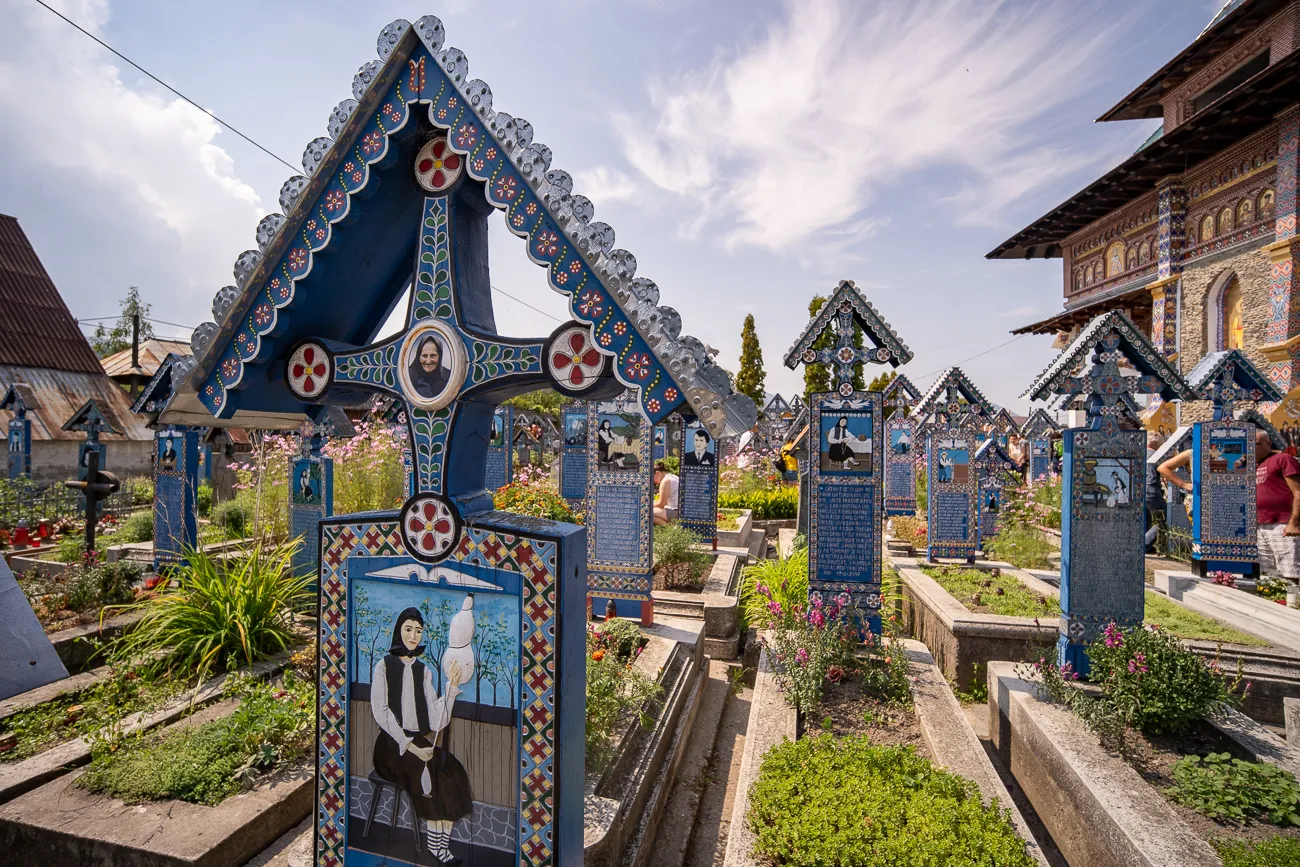 Farbenfrohe bemalte Grabkreuze in einem Friedhof unter blauem Himmel.