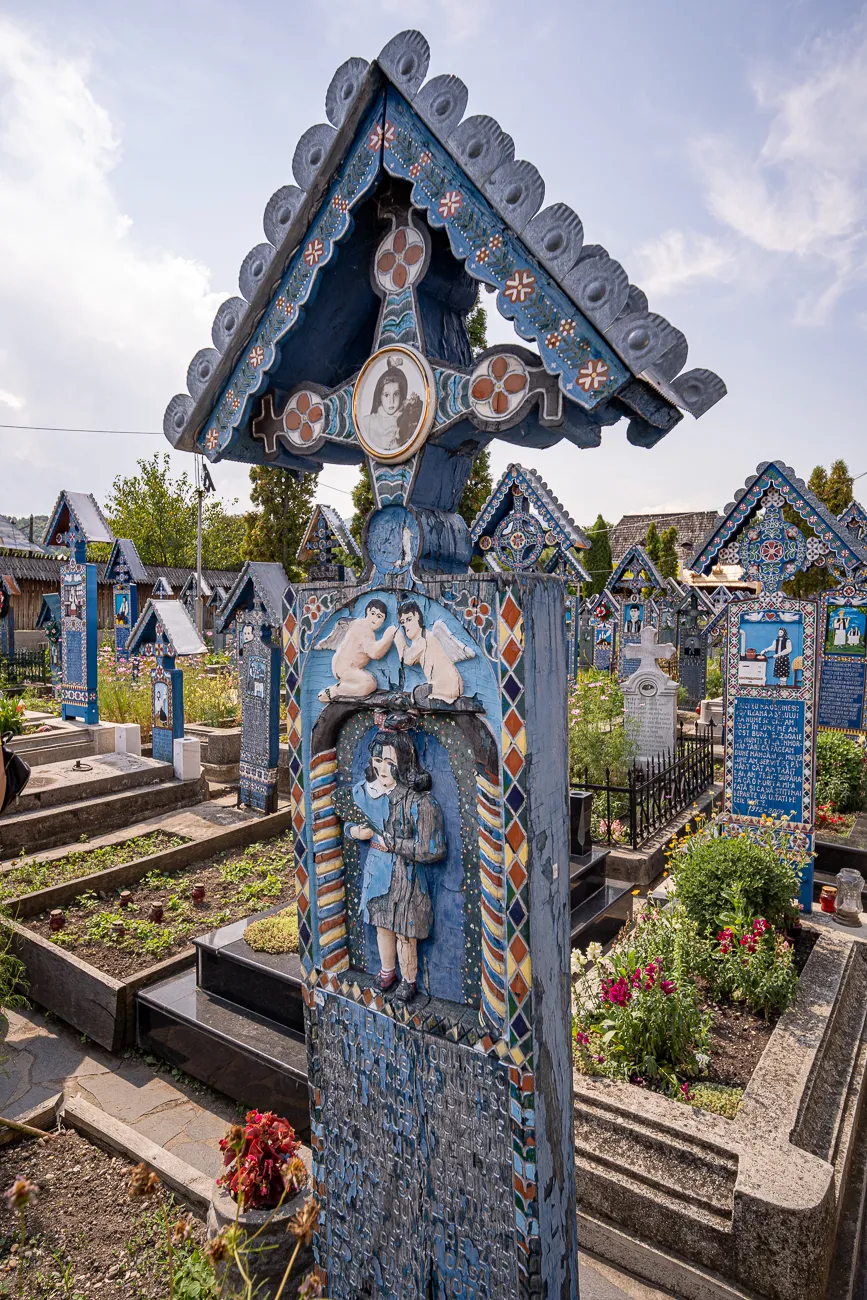 Farbenfroher blauer Grabstein mit Ornamenten und Figuren in einem Friedhof.