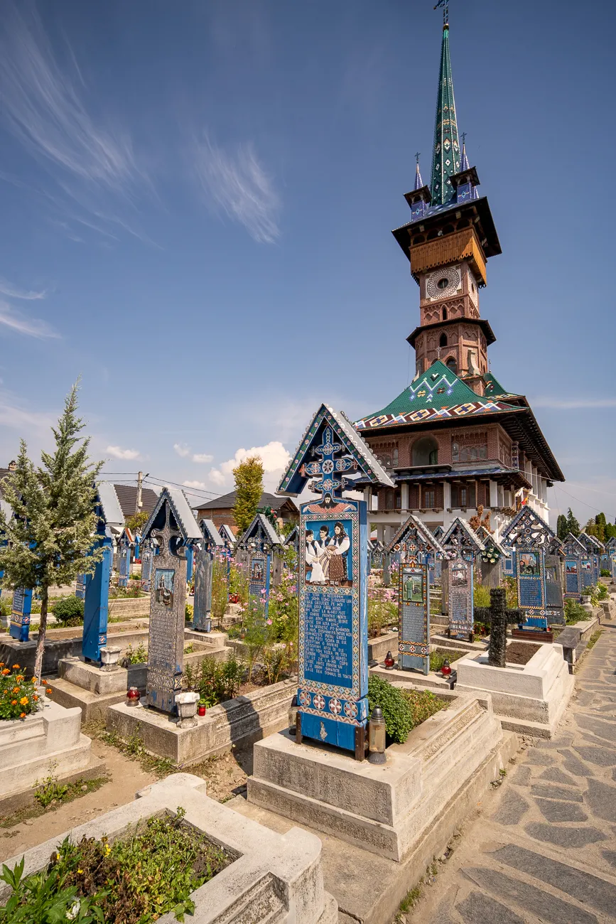 Farbige Grabsteine und Holzkirche im Friedhof unter blauem Himmel.