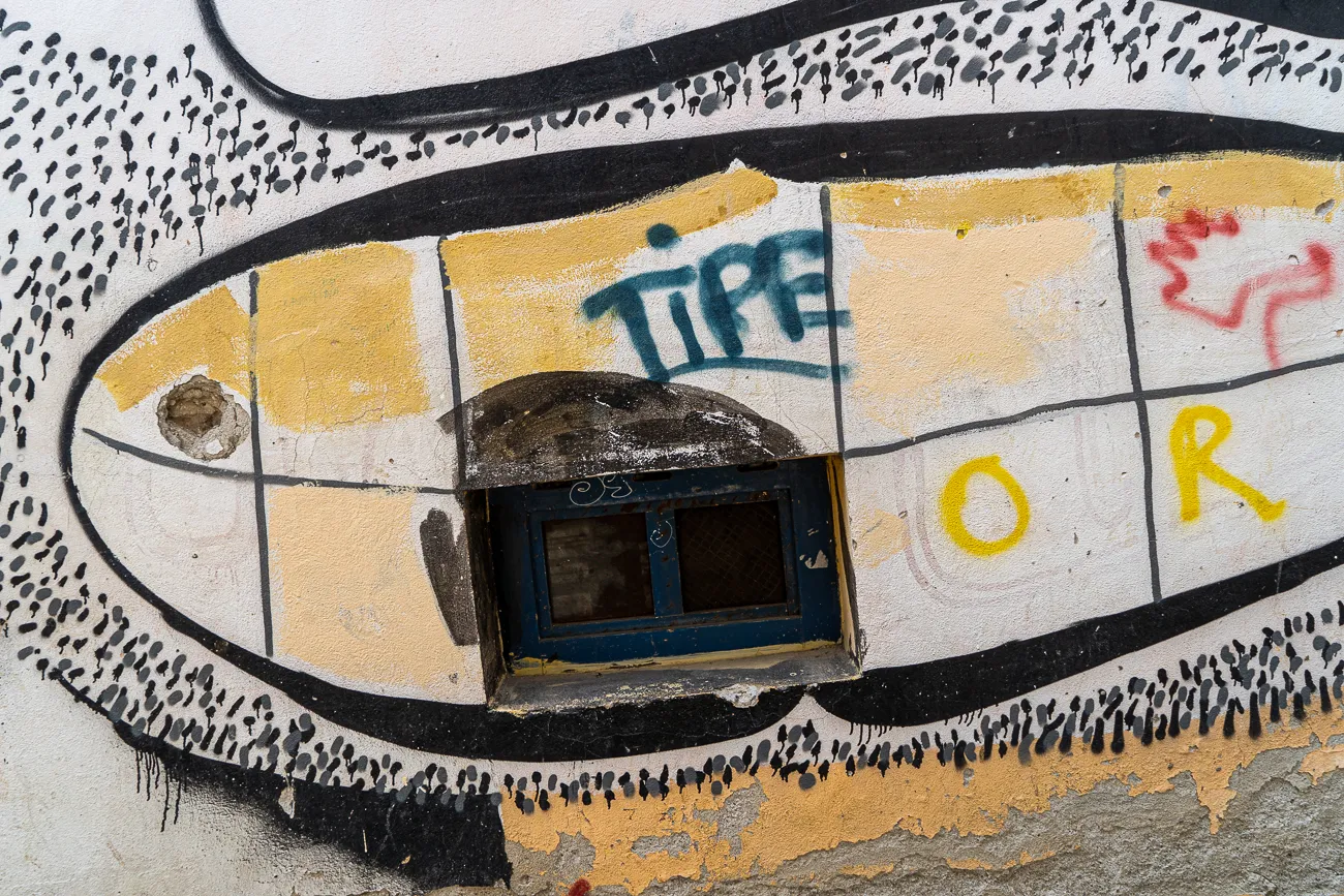 Graffiti an Wand mit blauem Fenster und gelben Buchstaben
