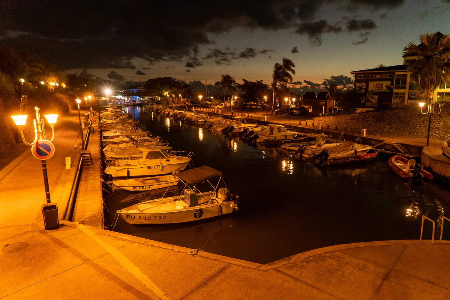Boote liegen im Hafen bei Dämmerung, Straßenlaternen werfen warmes Licht auf den Kai.