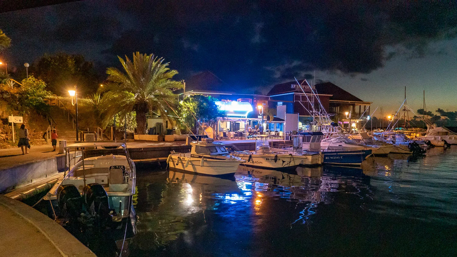 Boote im Hafen bei Nacht mit Lichtern und Palmen