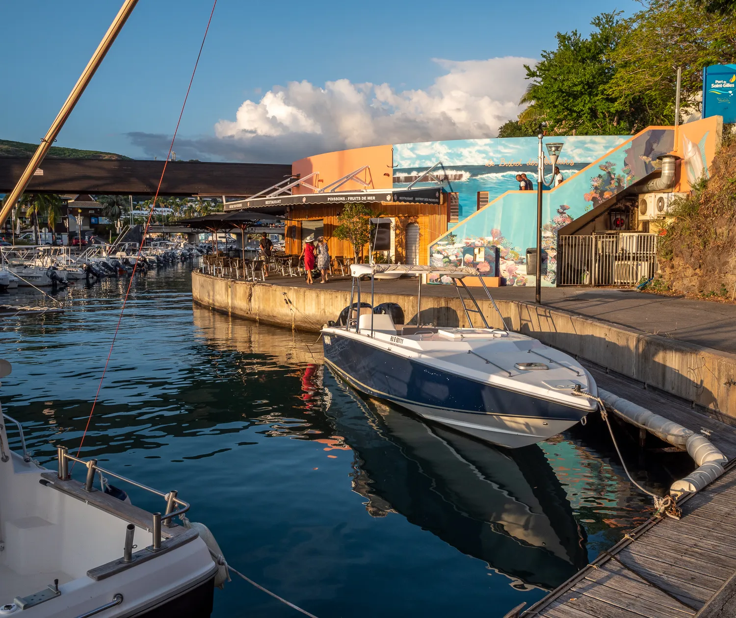 Boote liegen im Hafen, dahinter Strand und farbenfrohe Wandmalerei.