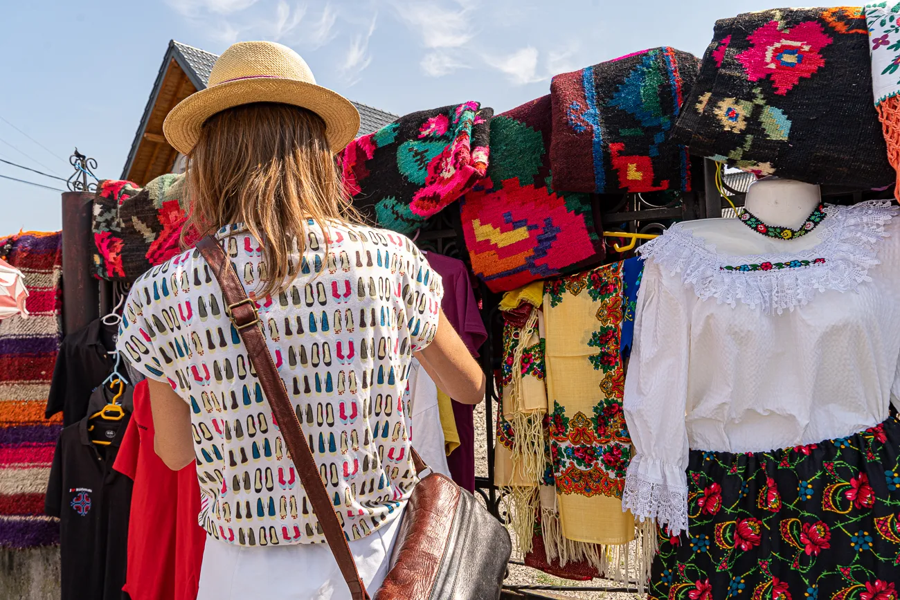 Frau mit Strohhut betrachtet farbenfrohe handgewebte Textilien und traditionelle Kleidung.