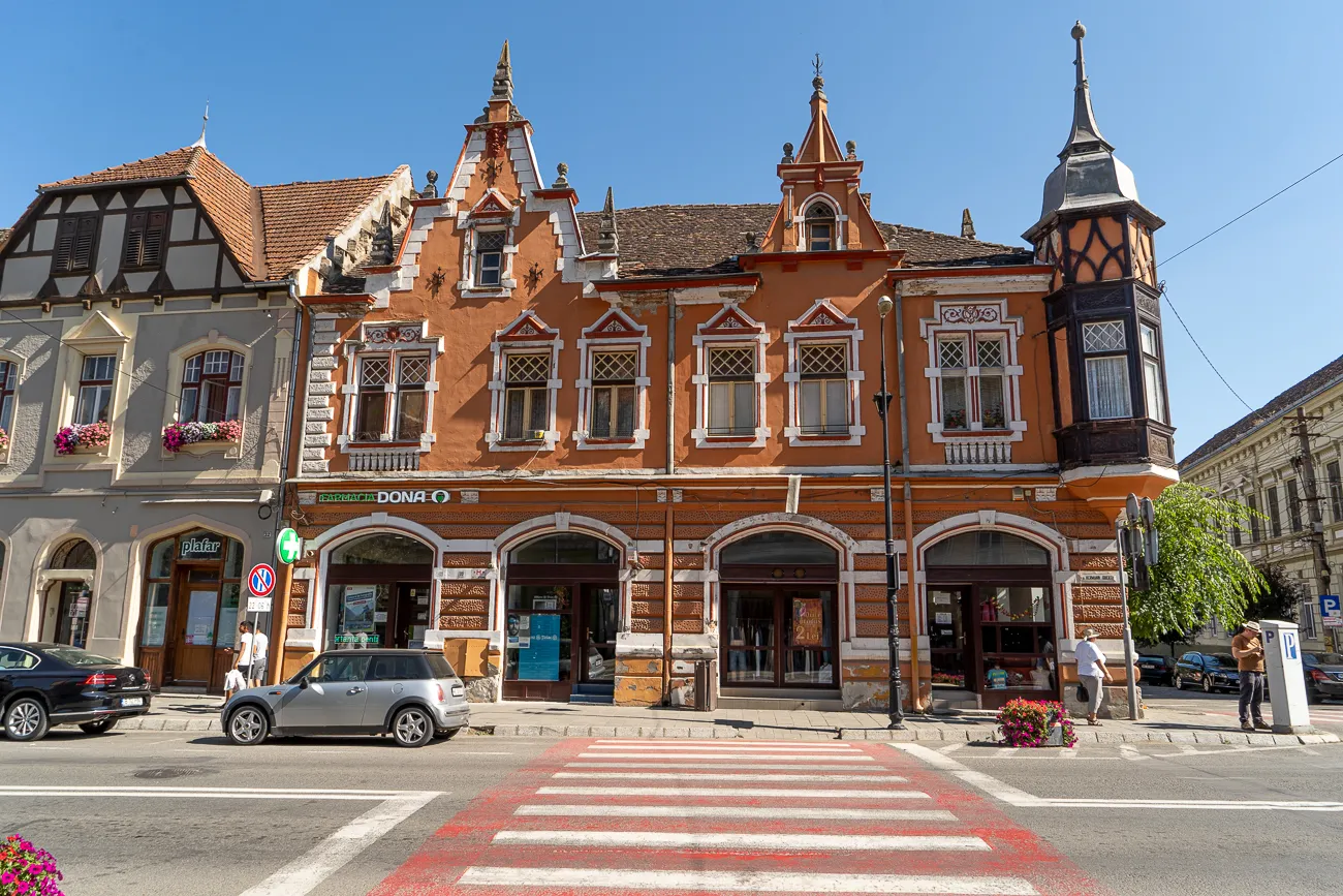 Ornate orange and white building with arched windows and a tower on a street corner.