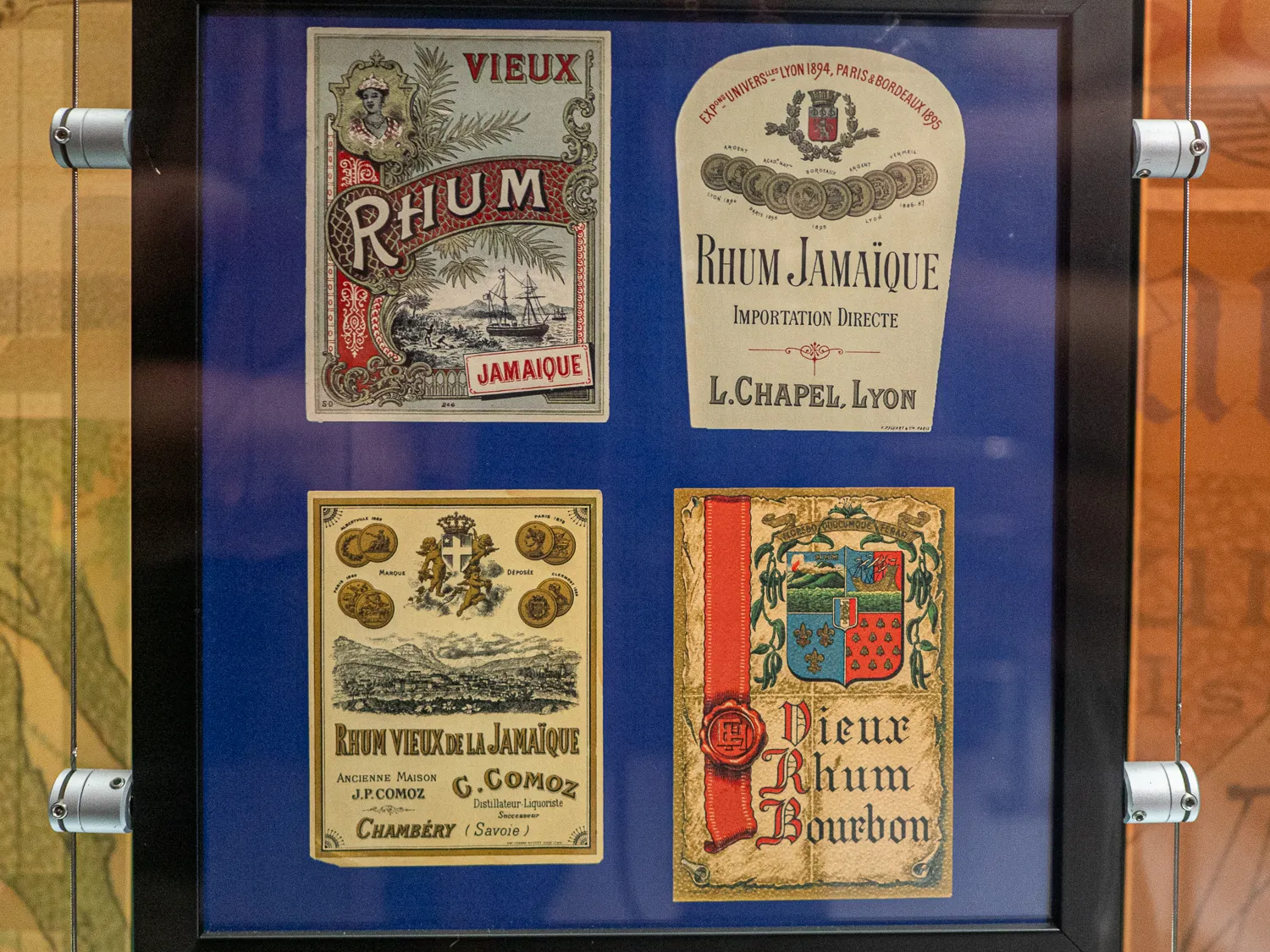 Vier historische Rumetiketten in einem Glasdisplay mit blauem Hintergrund.