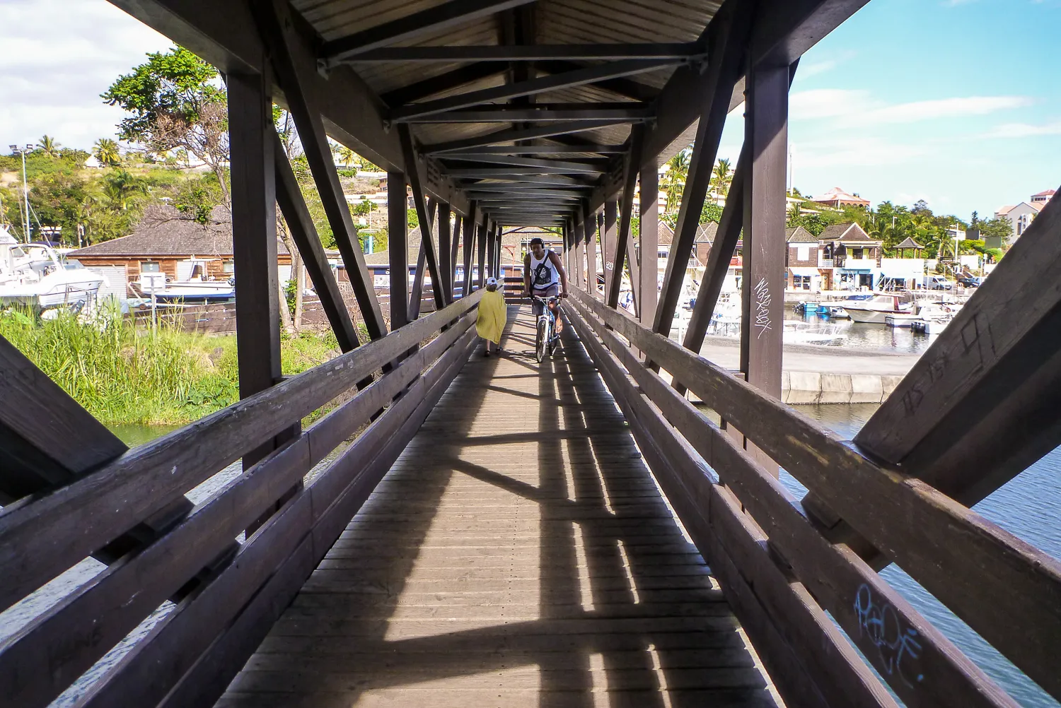 Zwei Personen gehen und fahren auf einer Holzbrücke über einen Hafen.