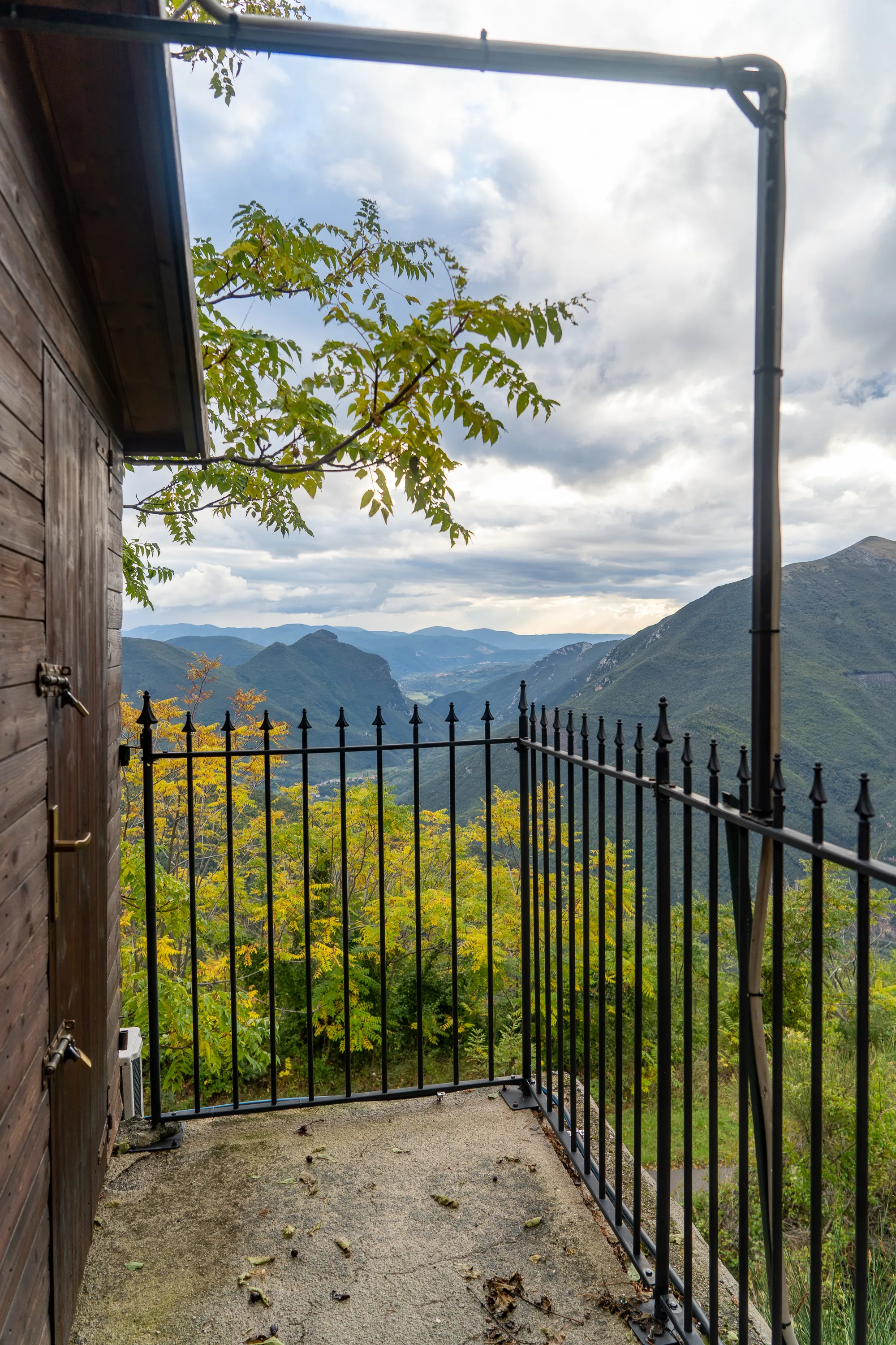 Holzhaus mit Balkon, Blick auf bewaldete Hügel unter bewölktem Himmel
