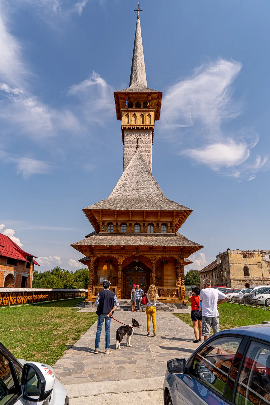 Holzkirche mit spitzen Turm unter blauem Himmel, Besucher und Hund auf Steinweg