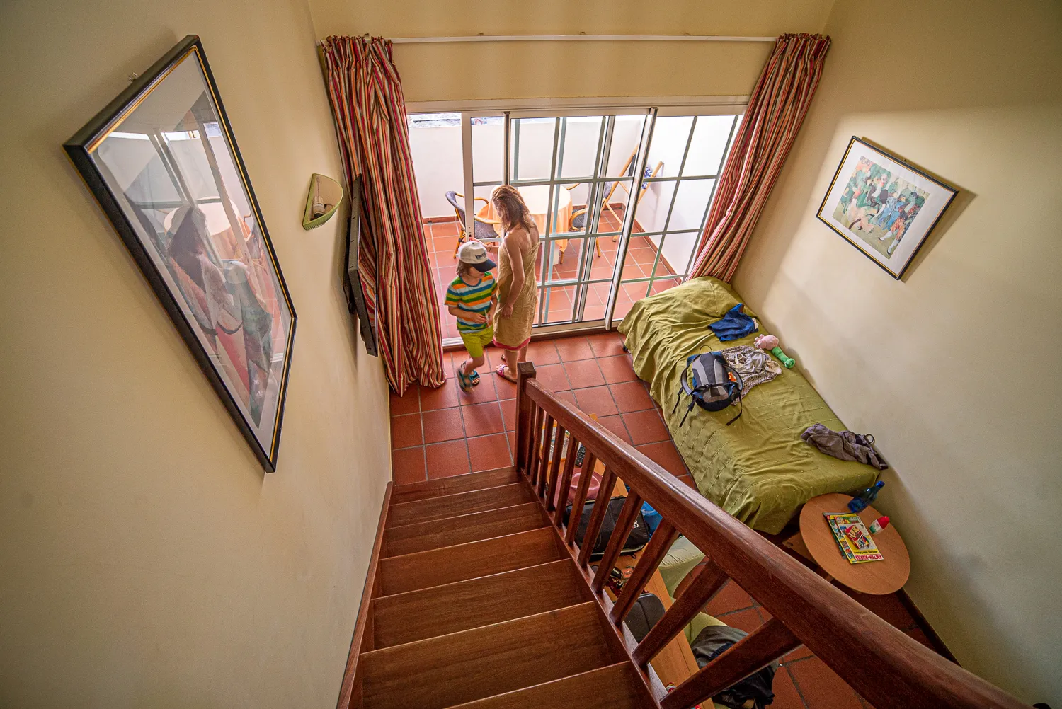 Zwei Kinder und eine Erwachsene stehen vor einer Glastür in einem Haus mit Holztreppe.
