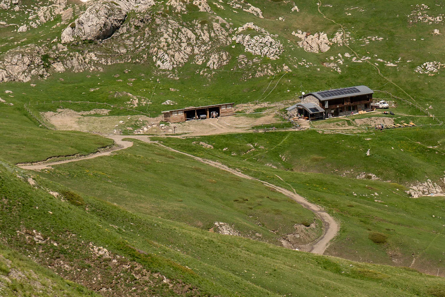 Hütte auf grüner Bergwiese mit Solaranlage und Wanderweg