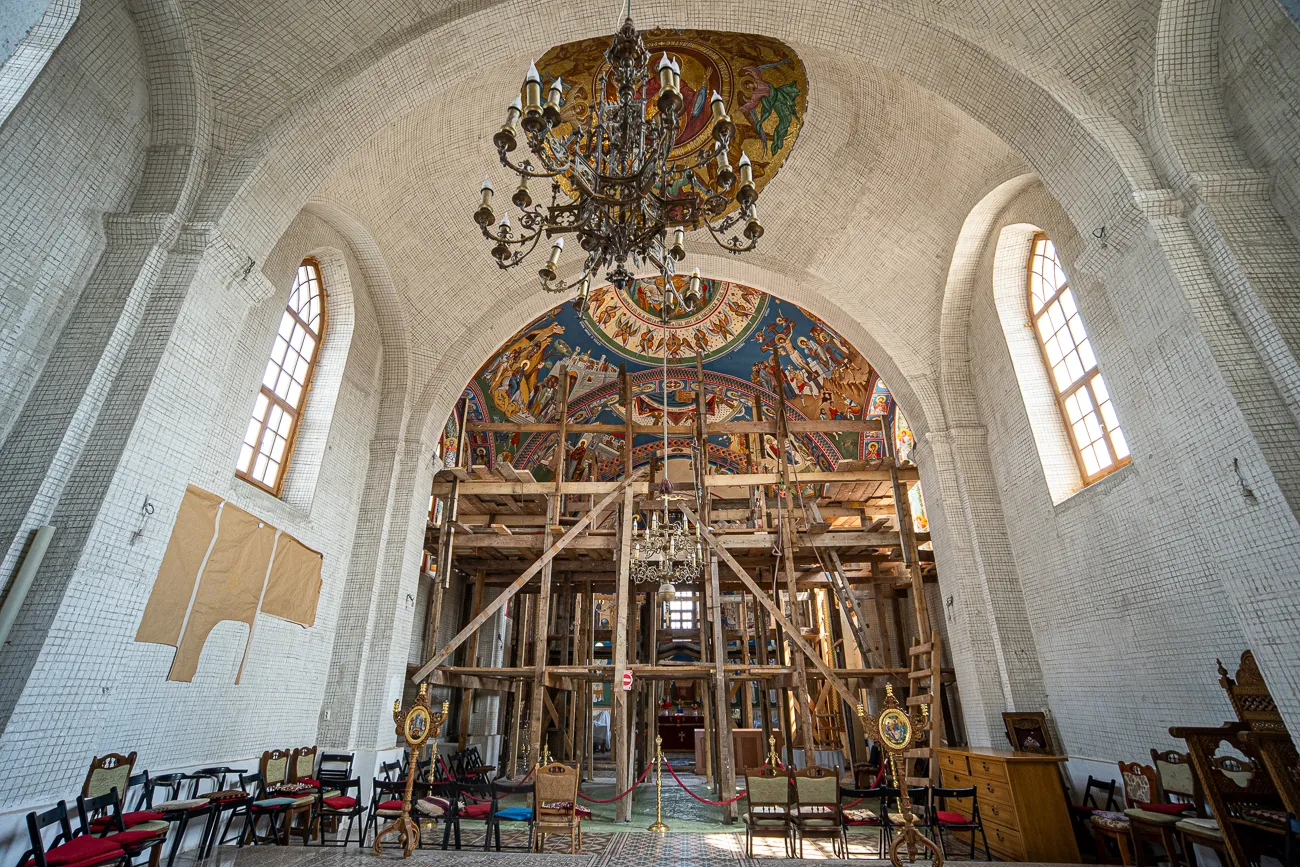 Innenraum einer Kirche mit Holzgerüst, Deckenmosaik und Kronleuchter