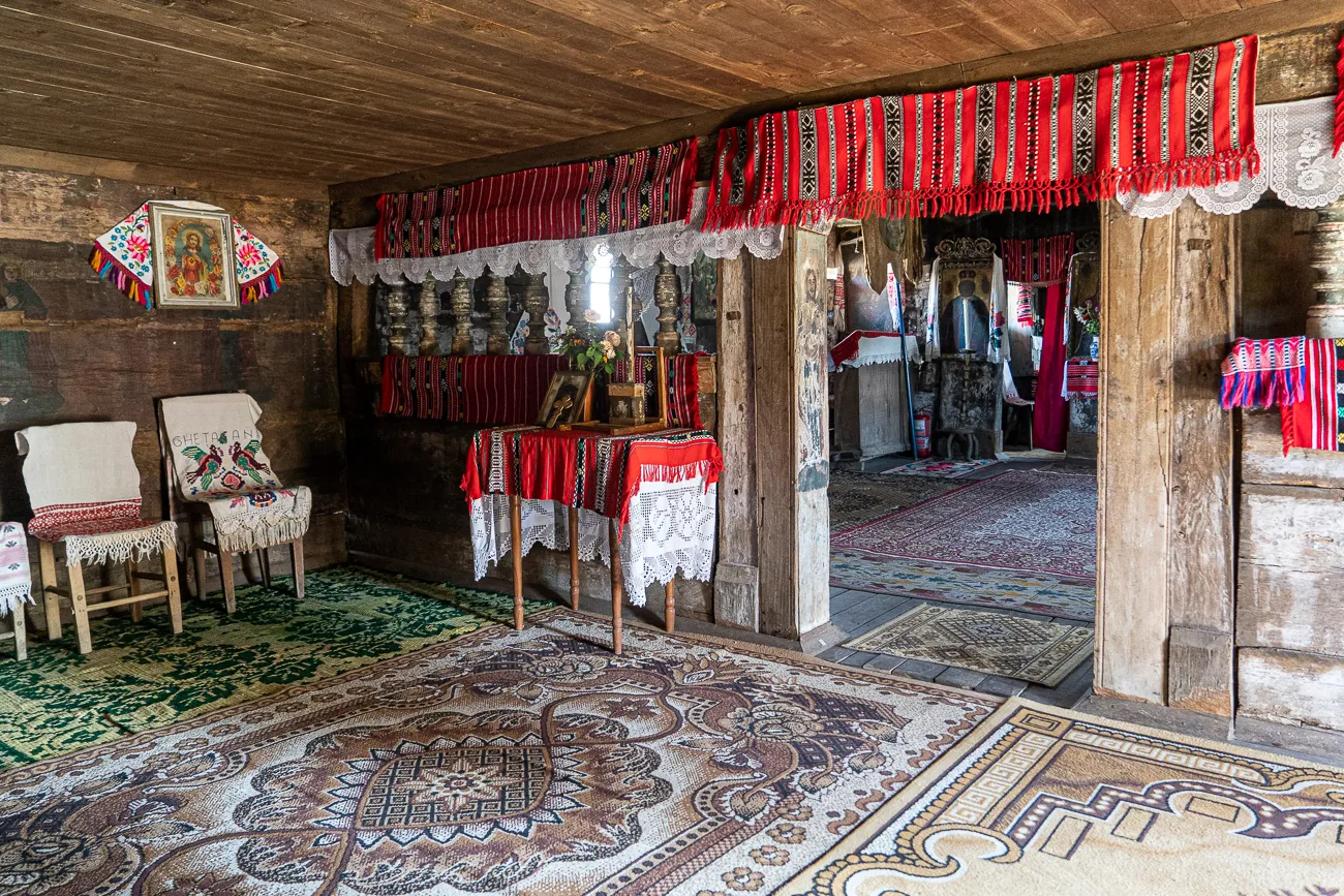 Innenraum einer Holzkirche mit bunten Teppichen und traditionellen Stickereien.