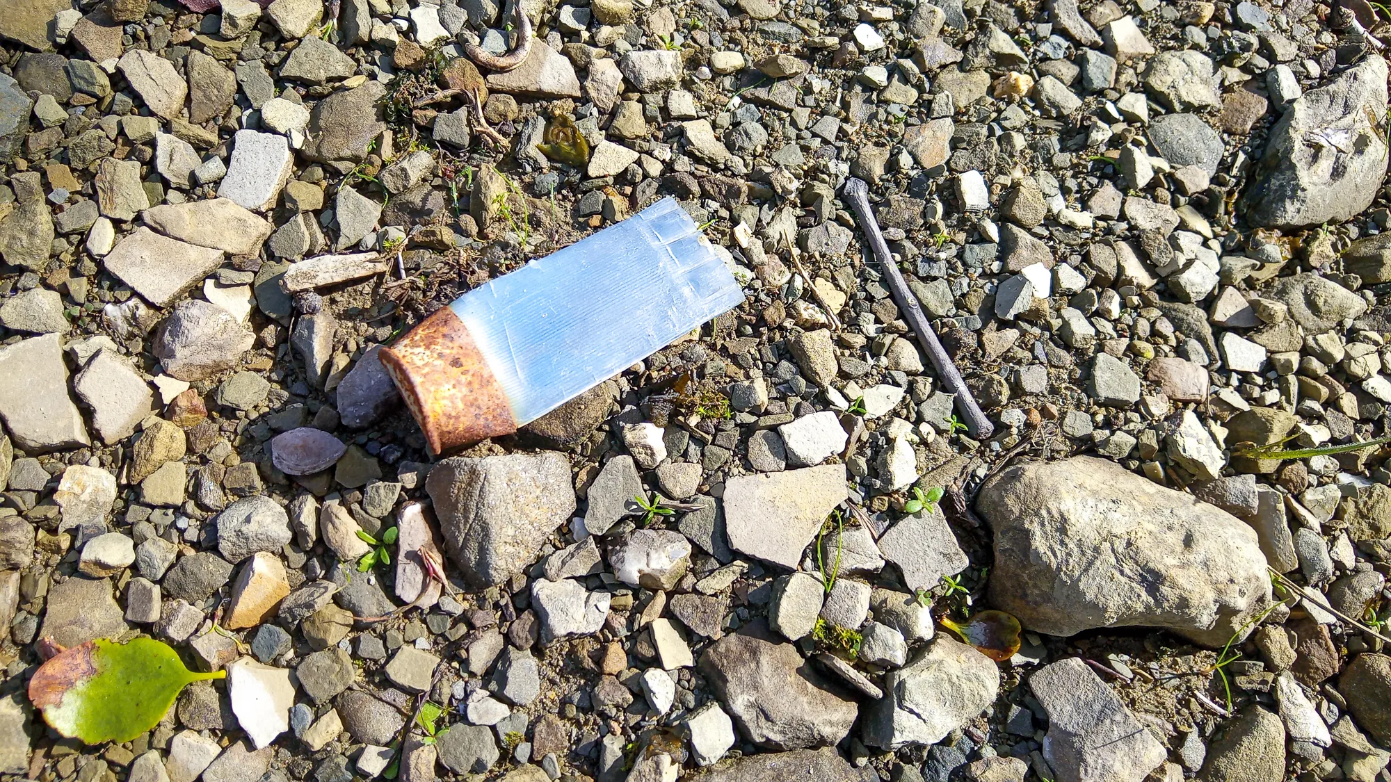 Kiesbank mit verrostetem Glasbehälter und Stab im Sonnenlicht