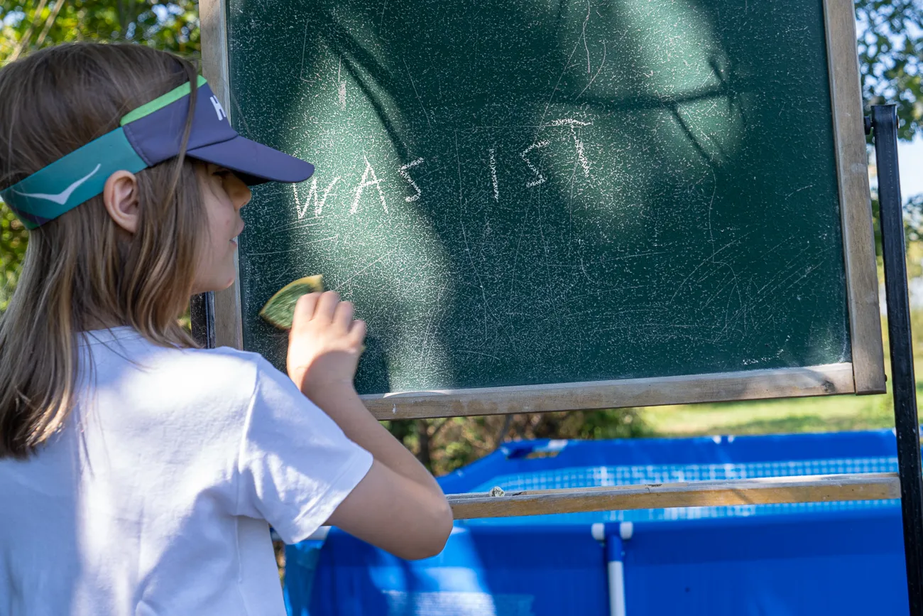 Kinderin schreibt mit Kreide auf grünes Brett im Freien