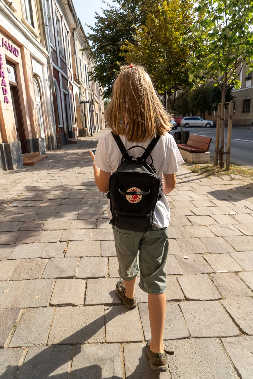 Kind mit Rucksack geht auf gepflastertem Gehweg in Stadt