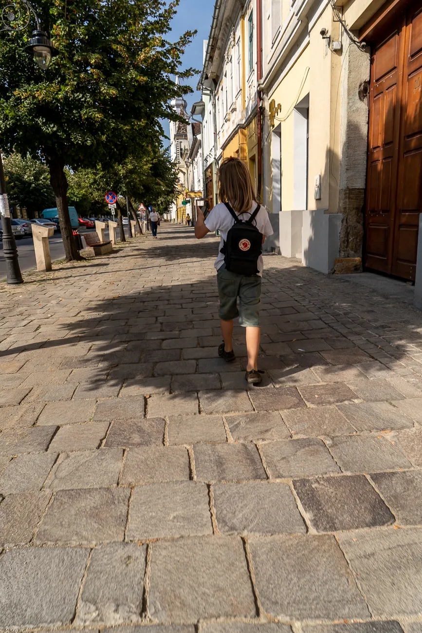 Kind mit Rucksack geht auf Kopfsteinpflasterweg in Stadt
