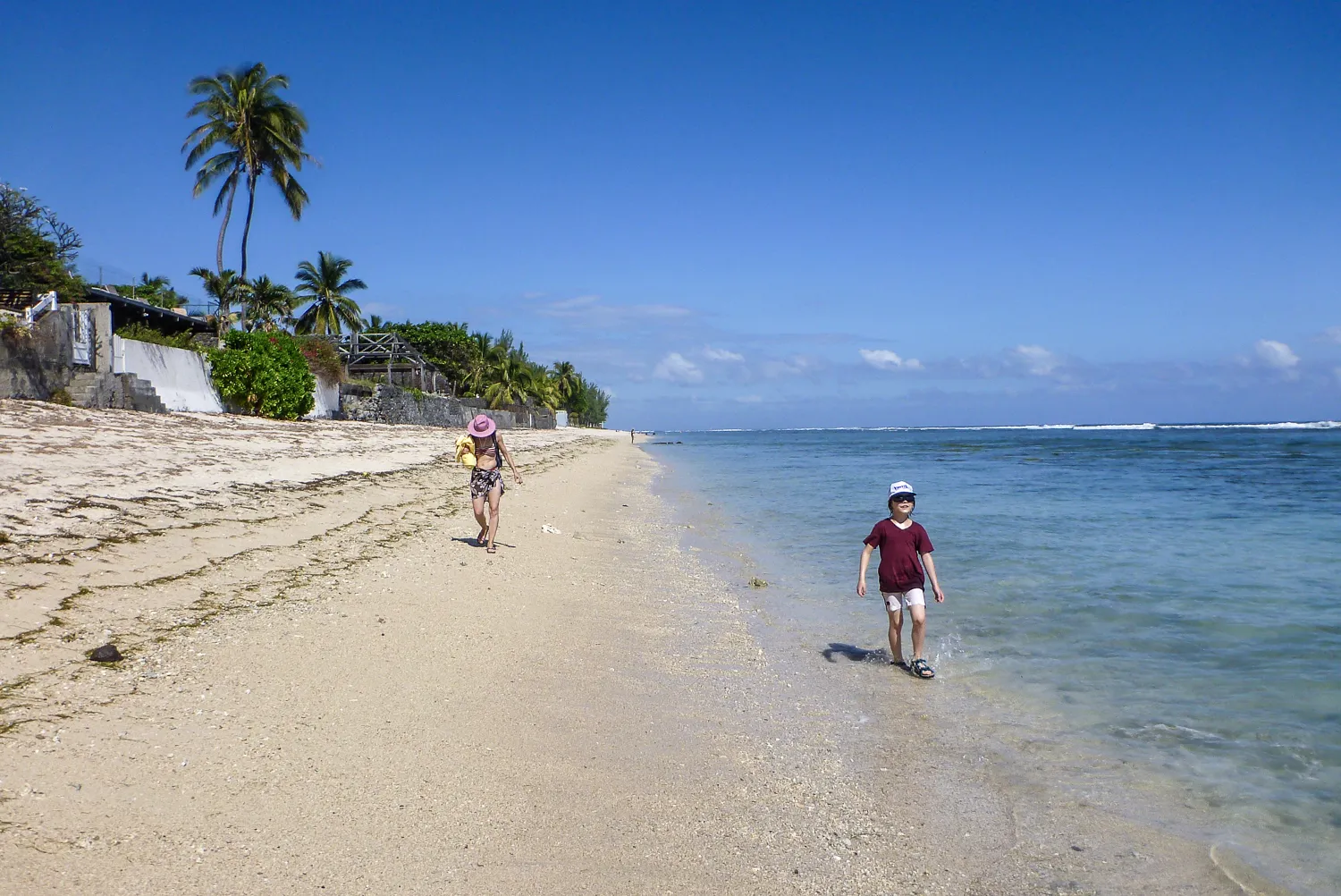 Zwei Kinder laufen am Strand entlang, einer im Wasser, der andere mit Schwimmring.