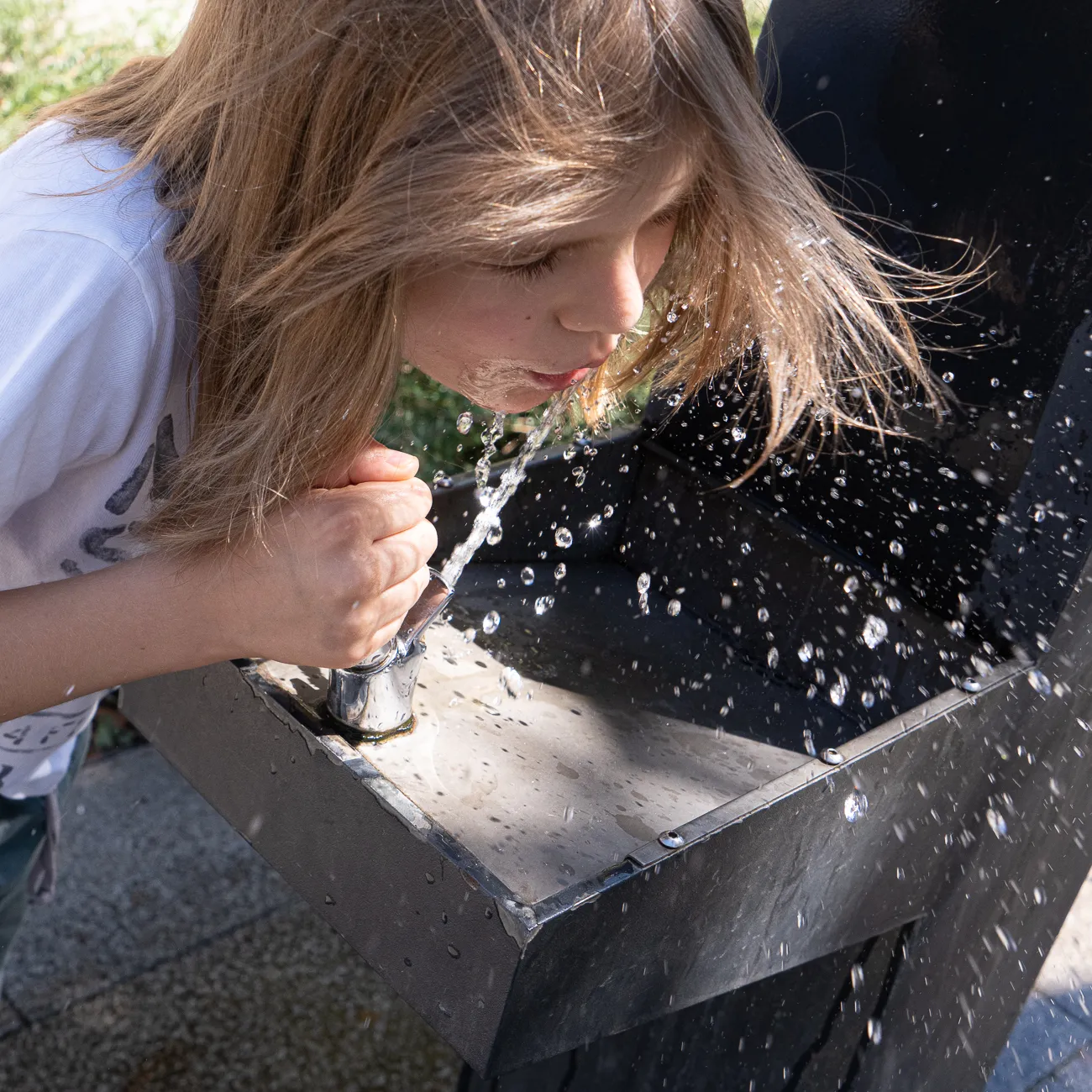 Kinderfrau trinkt aus einem Brunnen, Wasser spritzt umher.