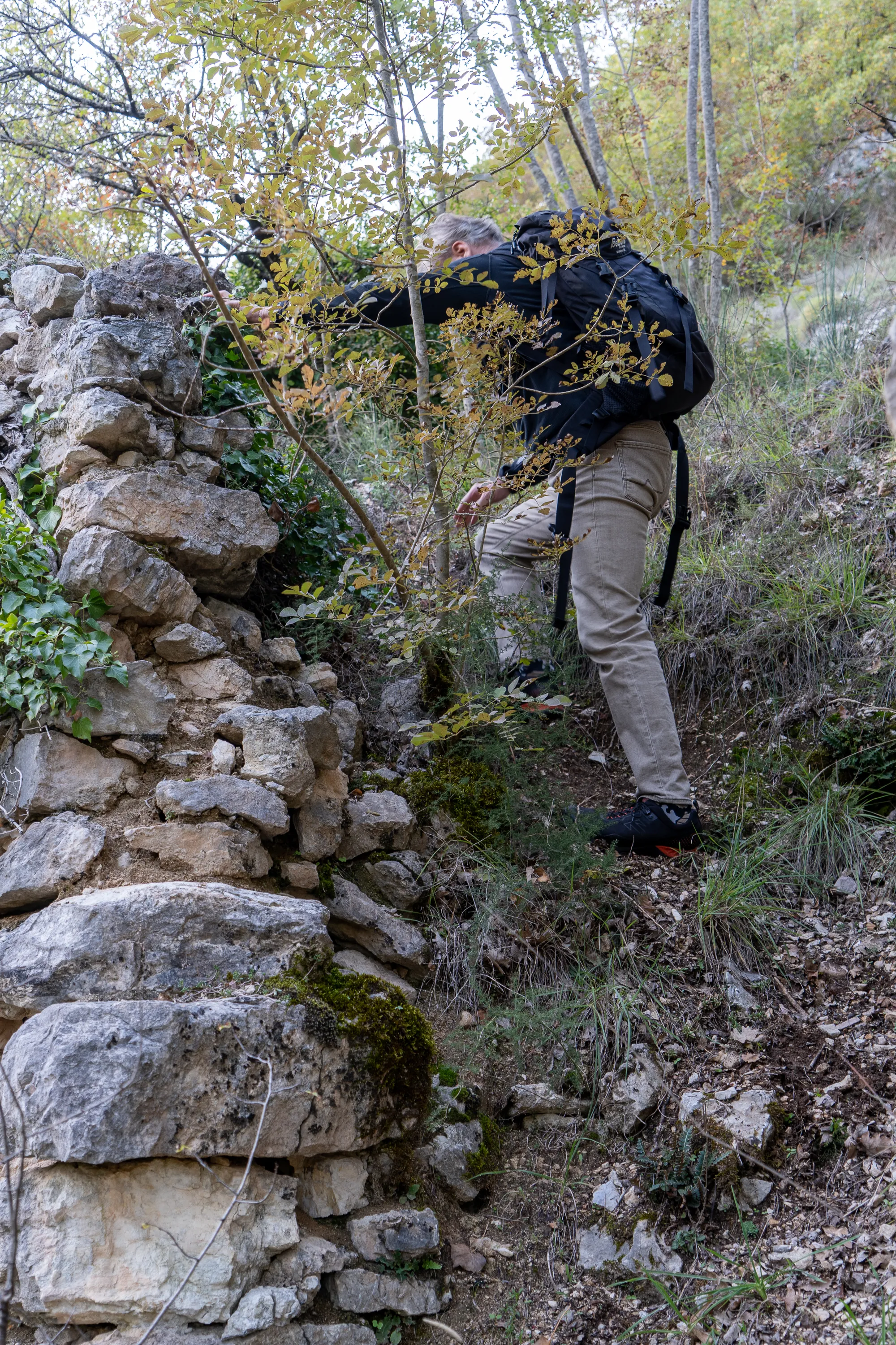 Mann mit Rucksack klettert an Steinmauer im Herbstwald