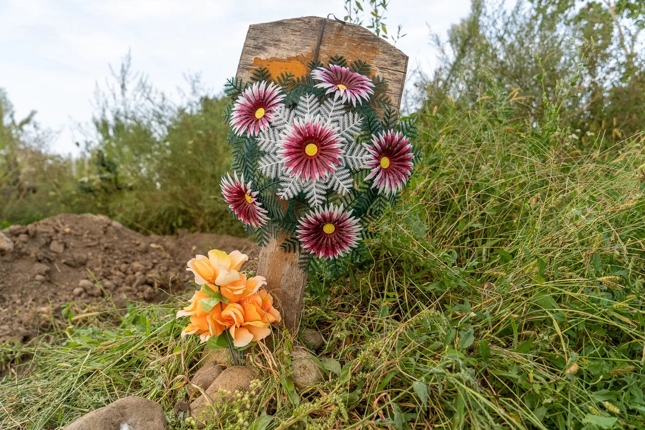 Künstliche Blumen an einem Holzpfosten im Gras
