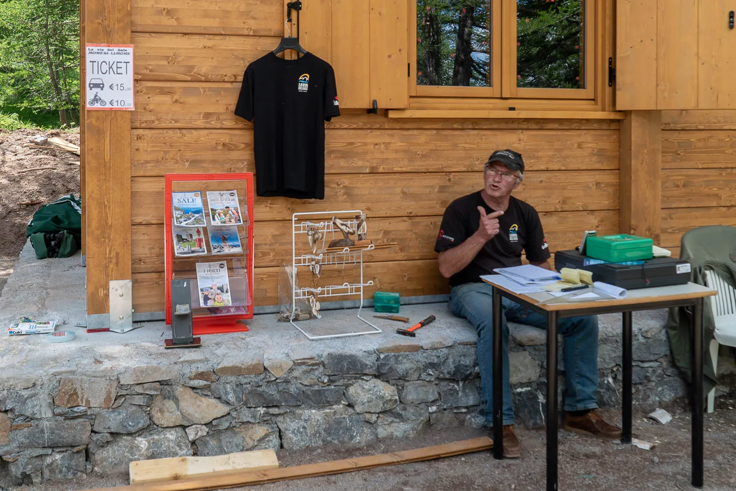Mann sitzt vor Holzhaus und zeigt mit Daumen nach oben