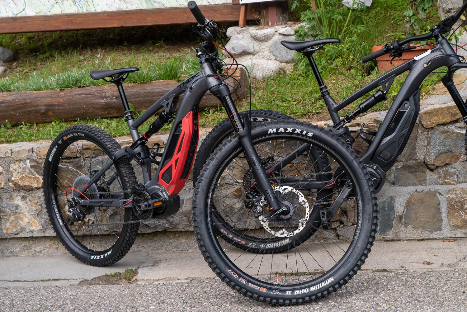 Zwei E-Bikes mit Maxxis-Reifen stehen an einer Steinmauer.