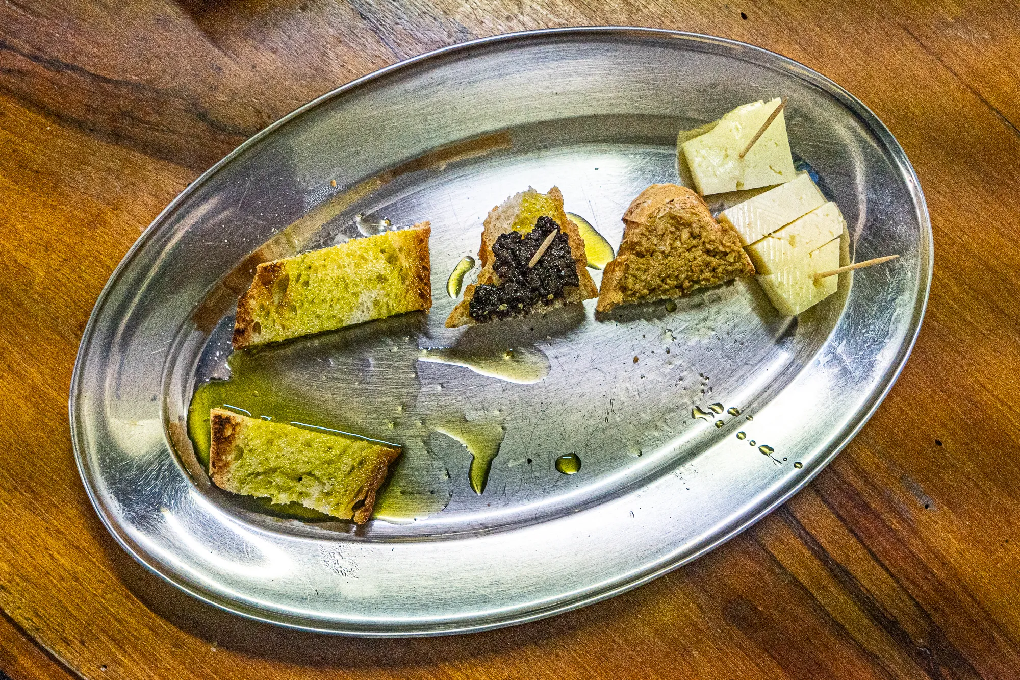 Metzgeressen auf silbernem Teller mit Olivenöl und Käse auf Holzoberfläche