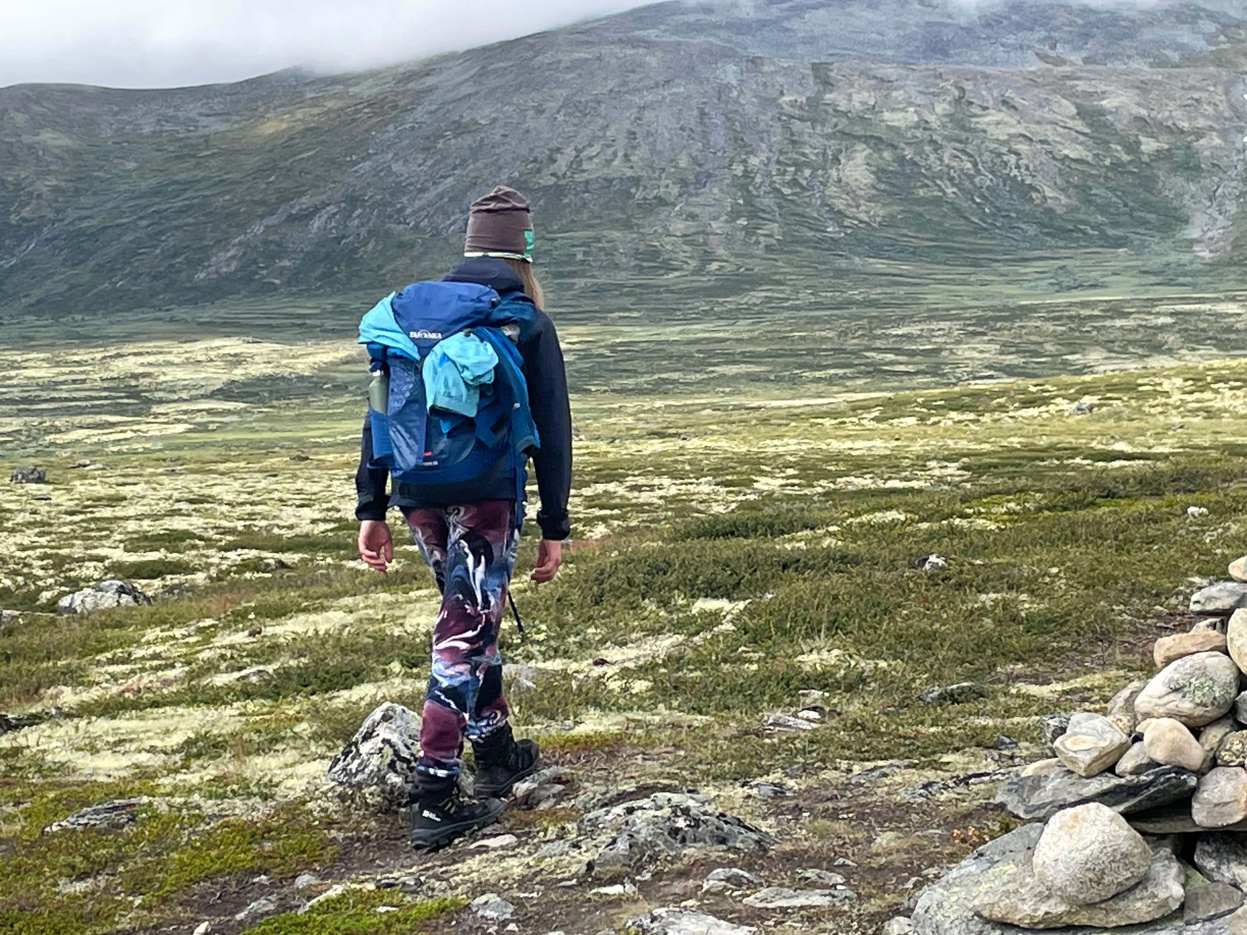 Mensch mit Rucksack wandert durch grüne Berglandschaft