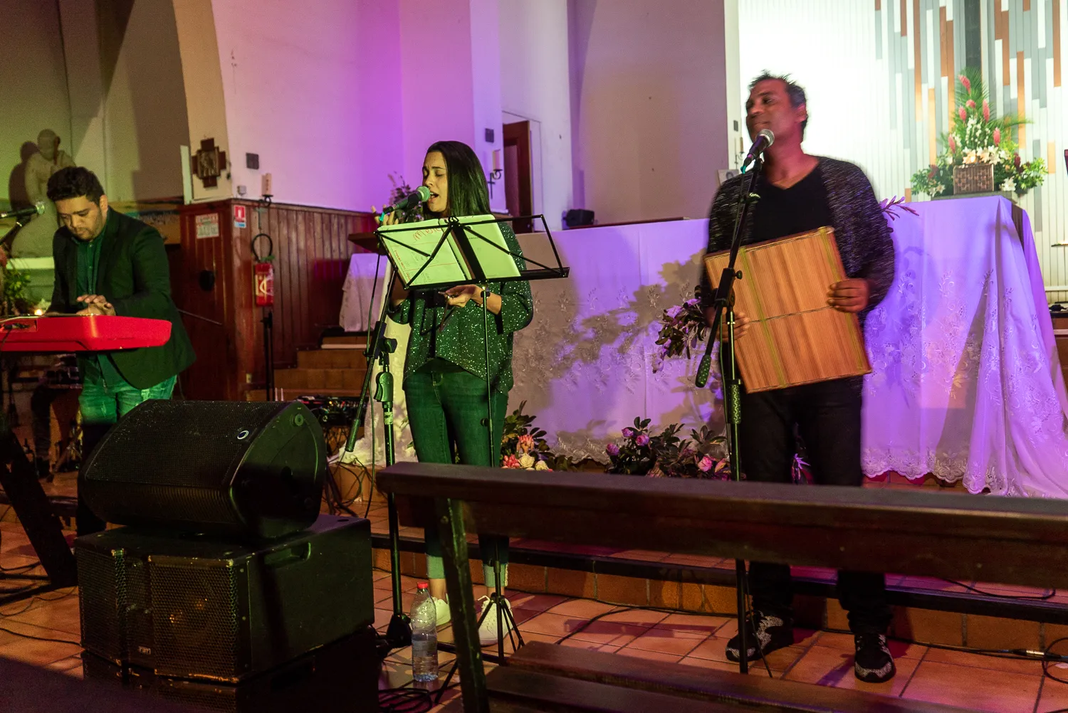 Drei Musiker spielen in einer Kirche mit Mikrofonen und Instrumenten.
