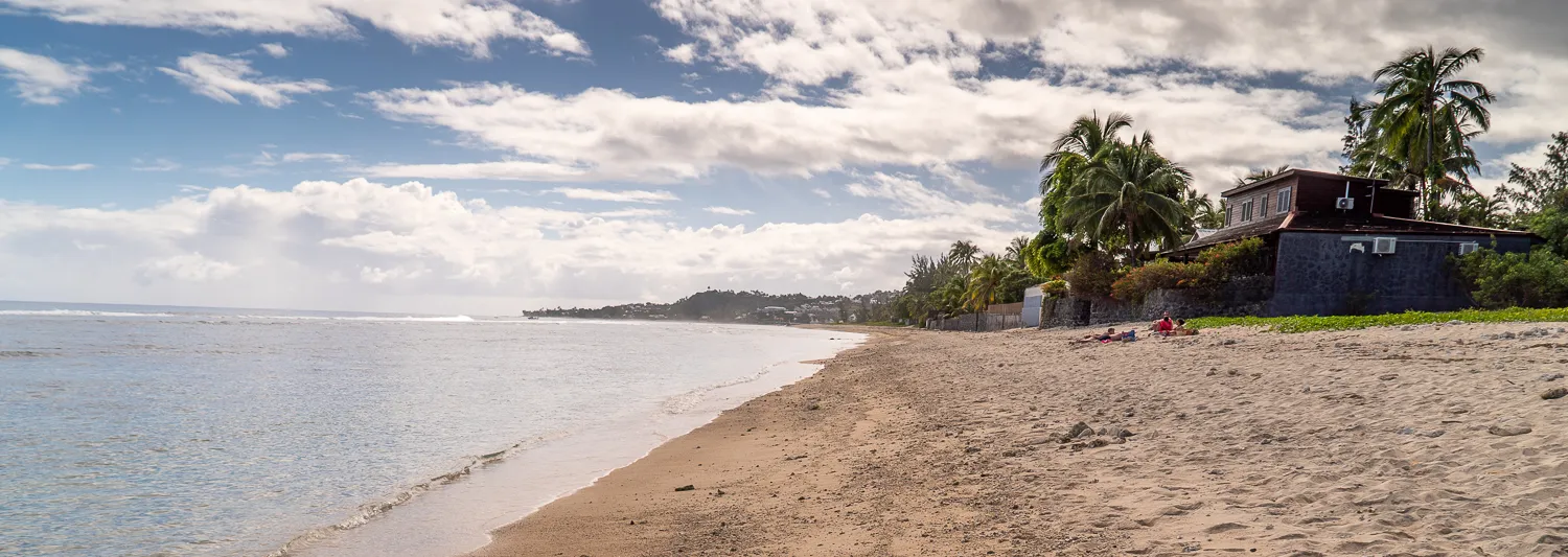 Strand mit Palmen und Häusern unter bewölktem Himmel