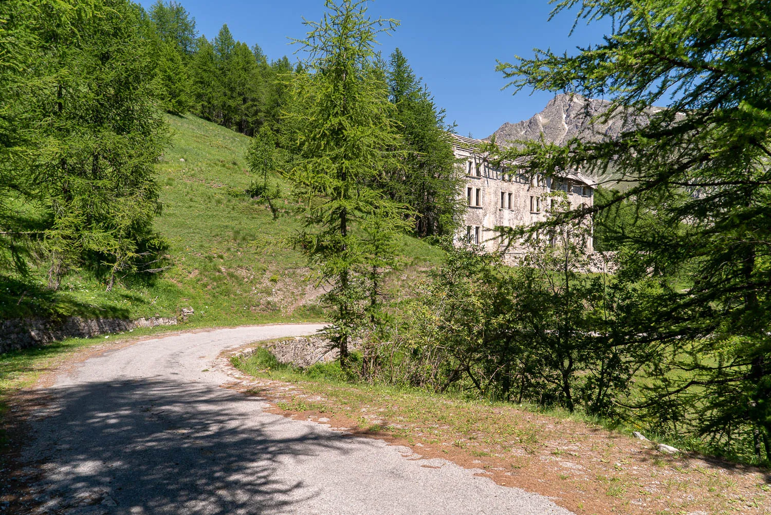 Gepflasterter Weg durch grüne Hügellandschaft mit altem Gebäude im Hintergrund.