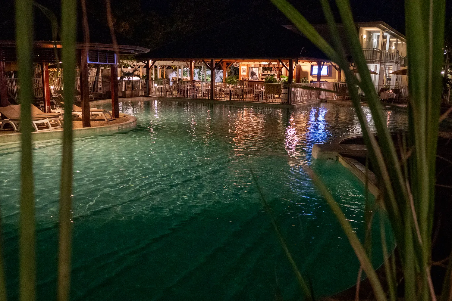 Nachts beleuchteter Pool mit Liegestühlen und Restaurant im Hintergrund
