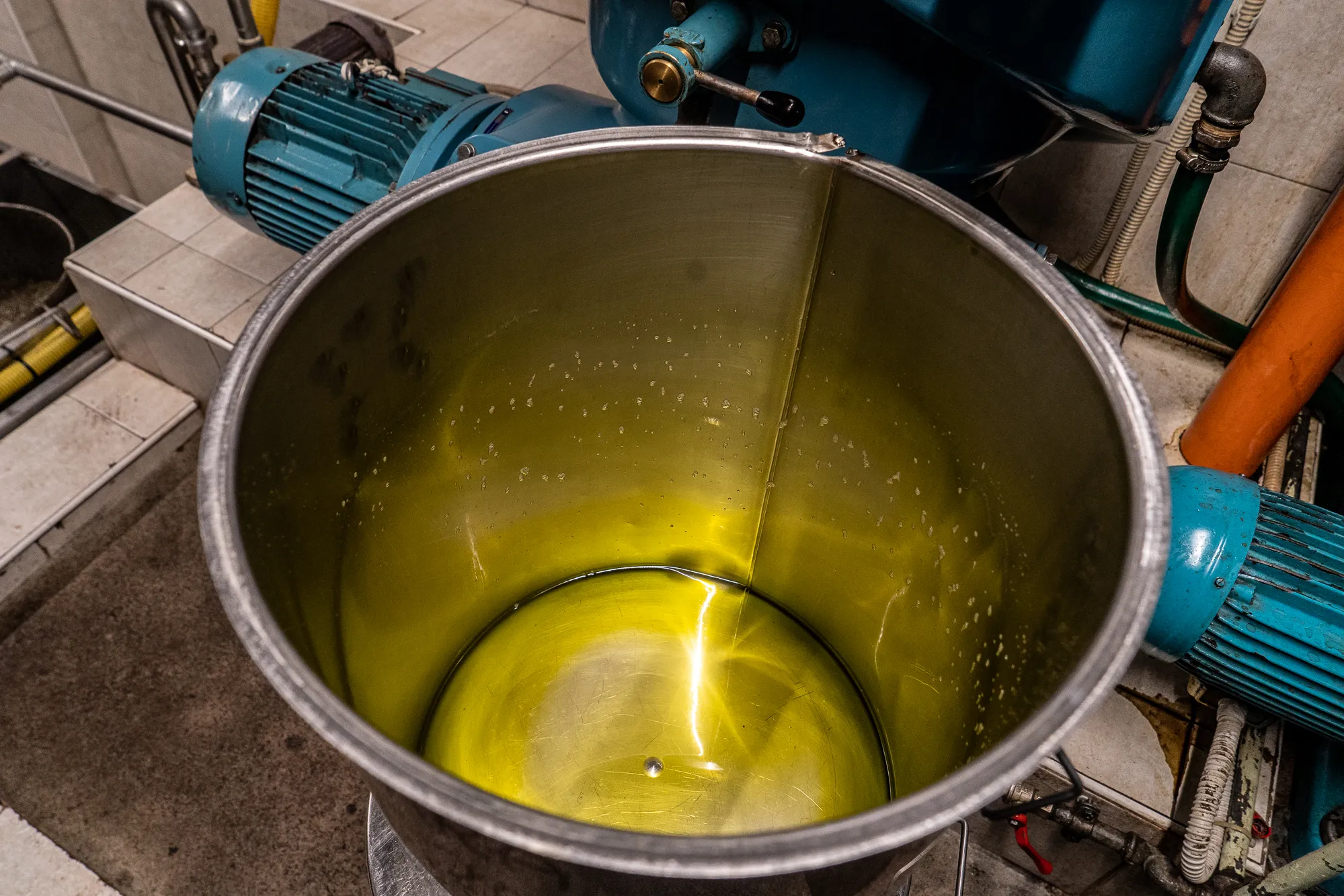 Metallbehälter mit gelbem Inhalt und blauen Pumpen im Hintergrund