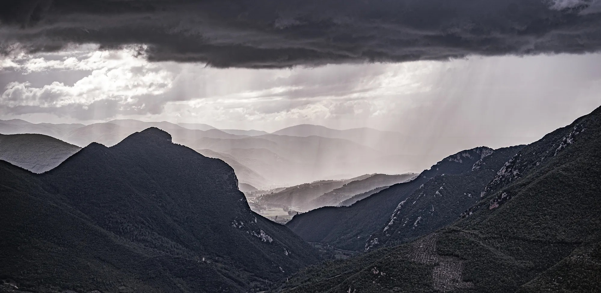 Berglandschaft mit Regenwolken und Sonnenstrahlen zwischen den Hügeln